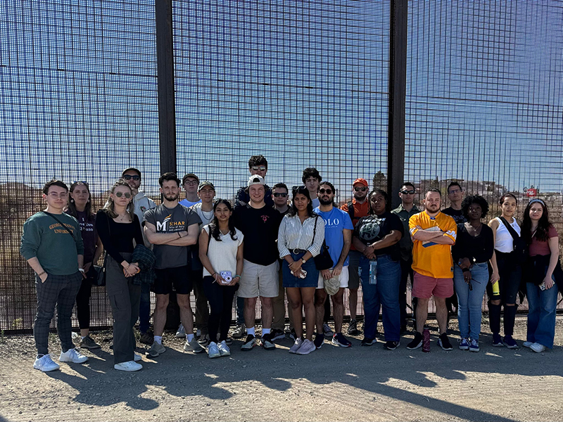 A group of students stand in front of a screened wall.