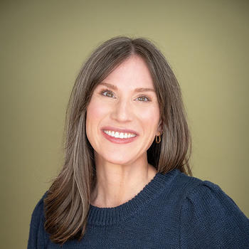 A woman with long brown hair in a dark top smiles at the camera.
